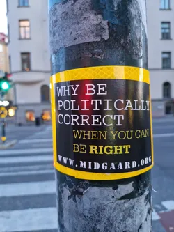 A sticker affixed to a pole, boldly proclaiming 'Why be politically correct when you can be right?'  The sticker features a yellow border and the website www.midgaard.org. The sticker's message is provocative and challenges the concept of political correctness.