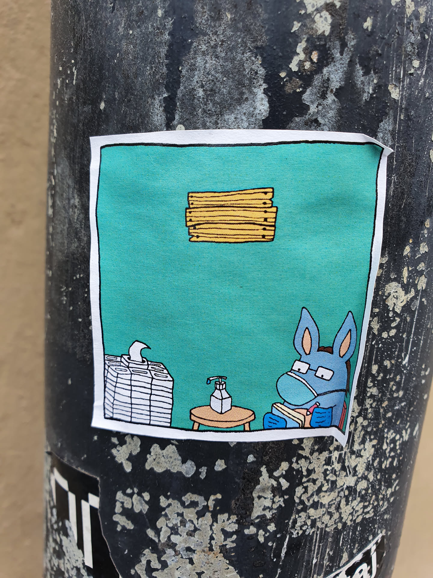 A sticker featuring a cartoon donkey wearing a facemask and reading a book, with hand sanitizer and tissues nearby. The scene is set against a teal background, with a stack of books or papers floating above.