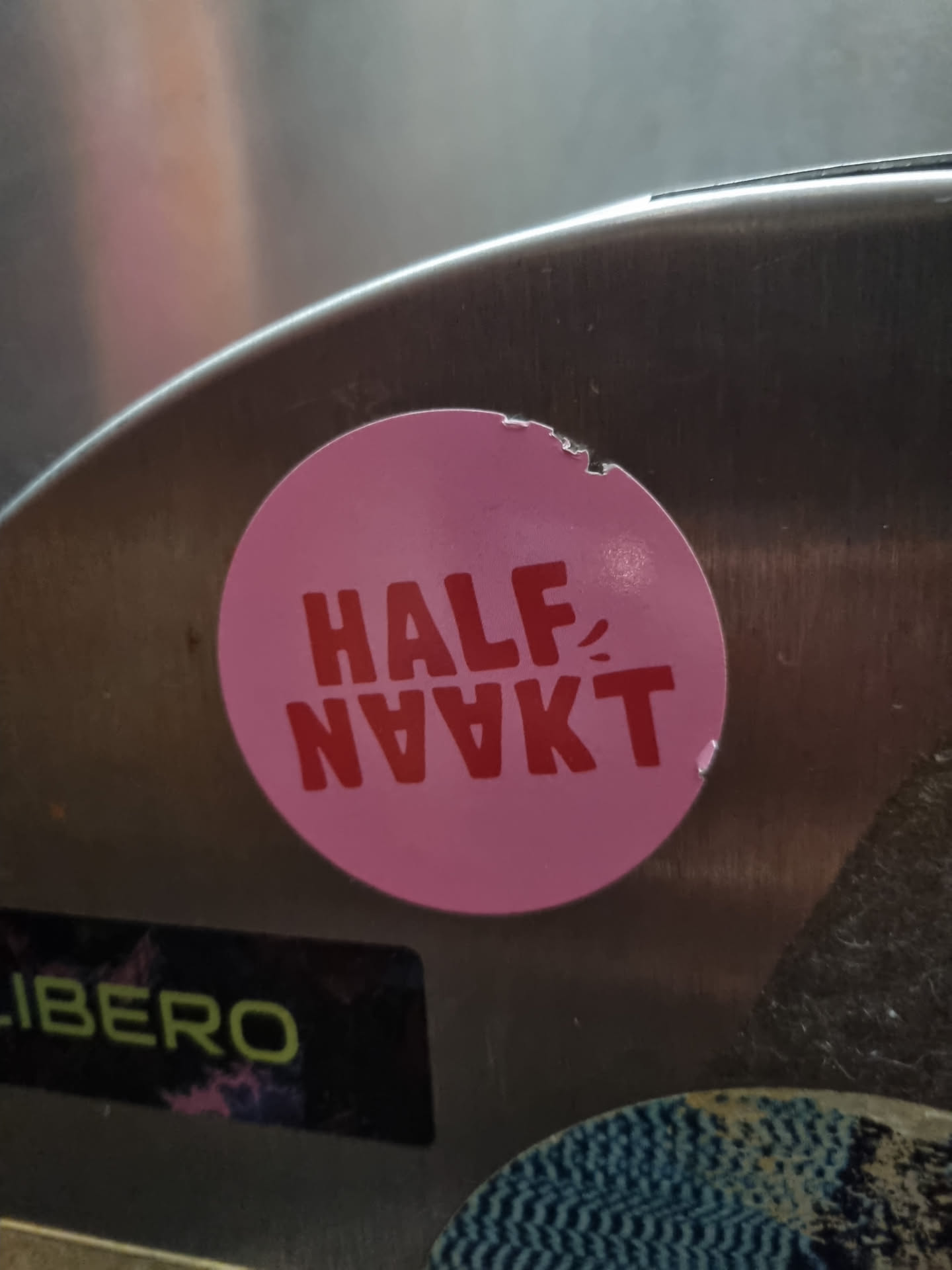 Pink round sticker with the text "HALF-NAAKT" in red. The sticker is slightly damaged.