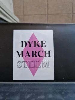 A sticker featuring the text "DYKE MARCH STHLM" with a pink diamond shape in the center. The sticker is adhered to a dark surface.