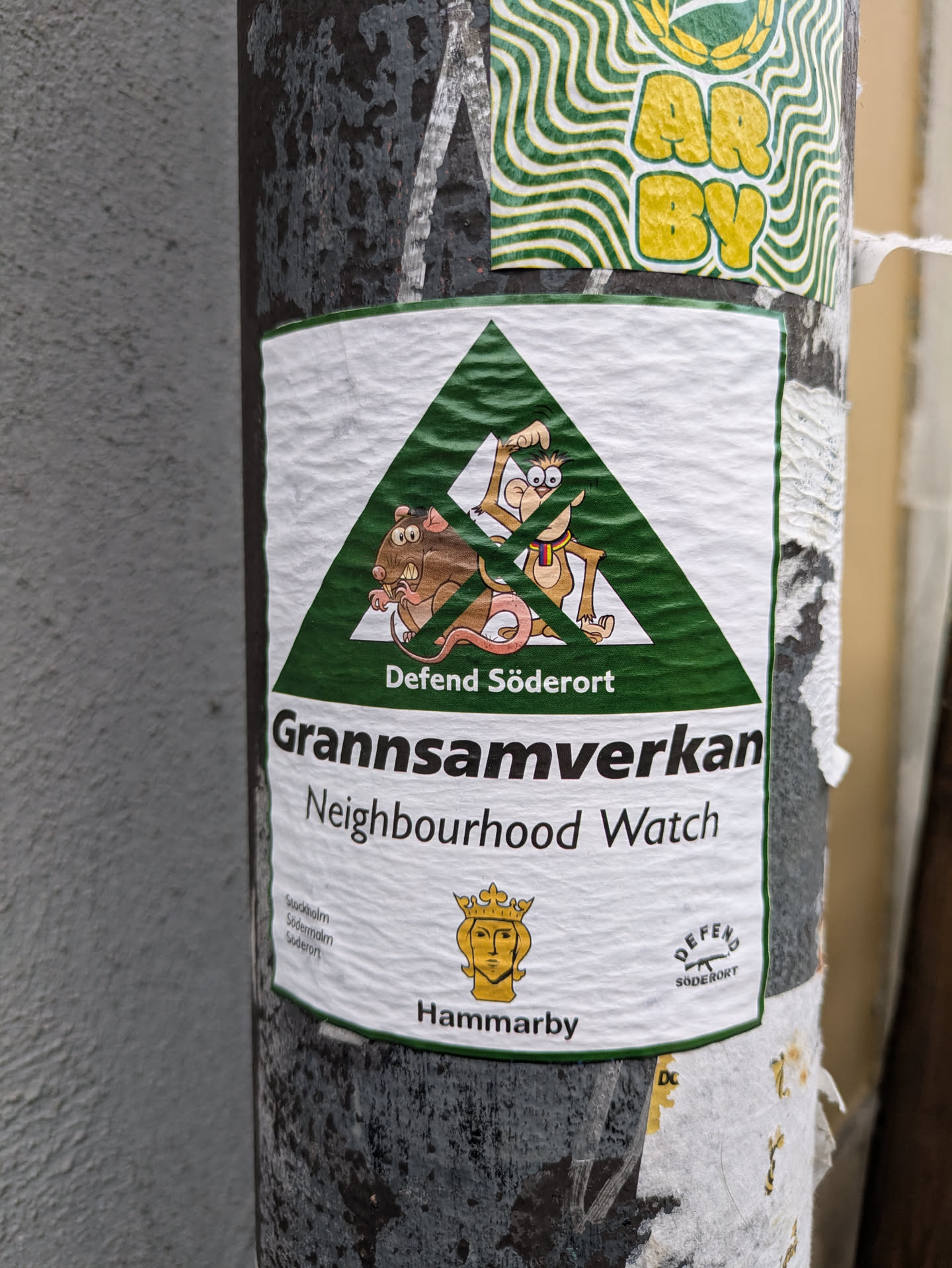 A green triangle sticker with cartoon rats and monkeys.  The text says "Gränsamverkan Neighbourhood Watch" and "Defend Söderort".  There is also a small Hammarby logo.