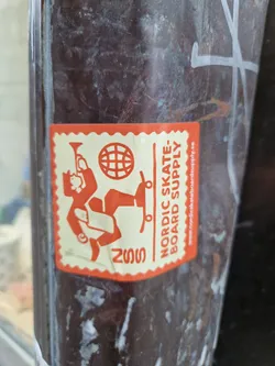 An orange sticker with a figure skateboarding and a globe. The text 'Nordic Skate: Board Supply' is visible, along with a website address. The year 2022 is also printed on the sticker.