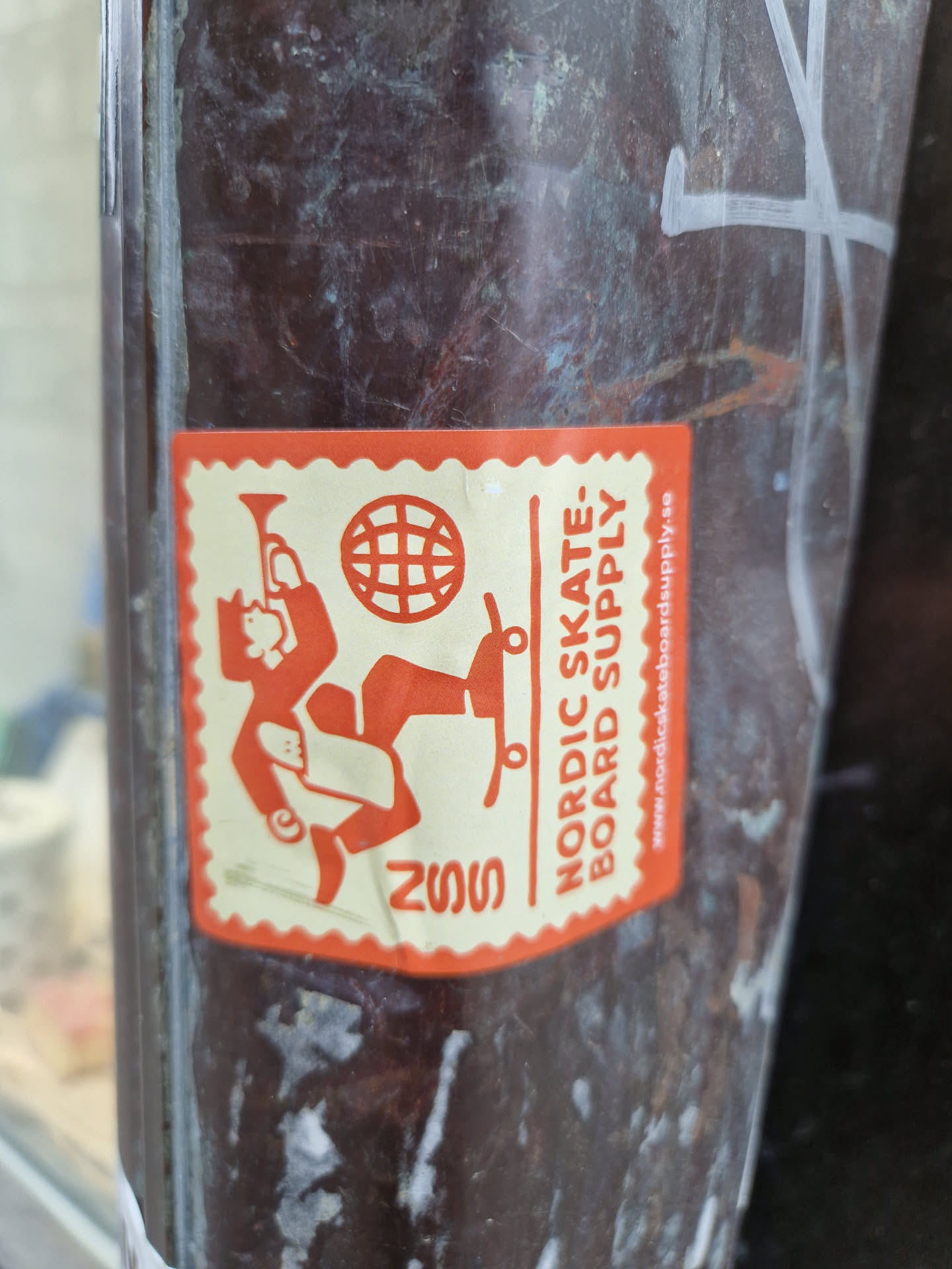 An orange sticker with a figure skateboarding and a globe. The text 'Nordic Skate: Board Supply' is visible, along with a website address. The year 2022 is also printed on the sticker.