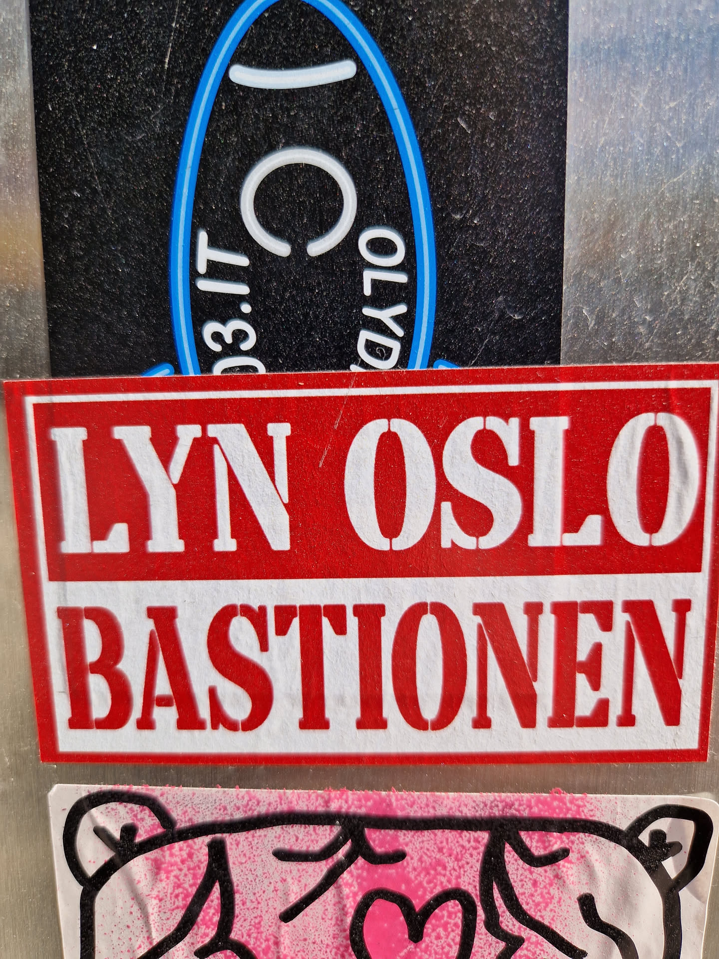 A red and white sticker with the text "LYN OSLO BASTIONEN" in a stencil-like font. It's affixed to a surface with other stickers visible in the background.