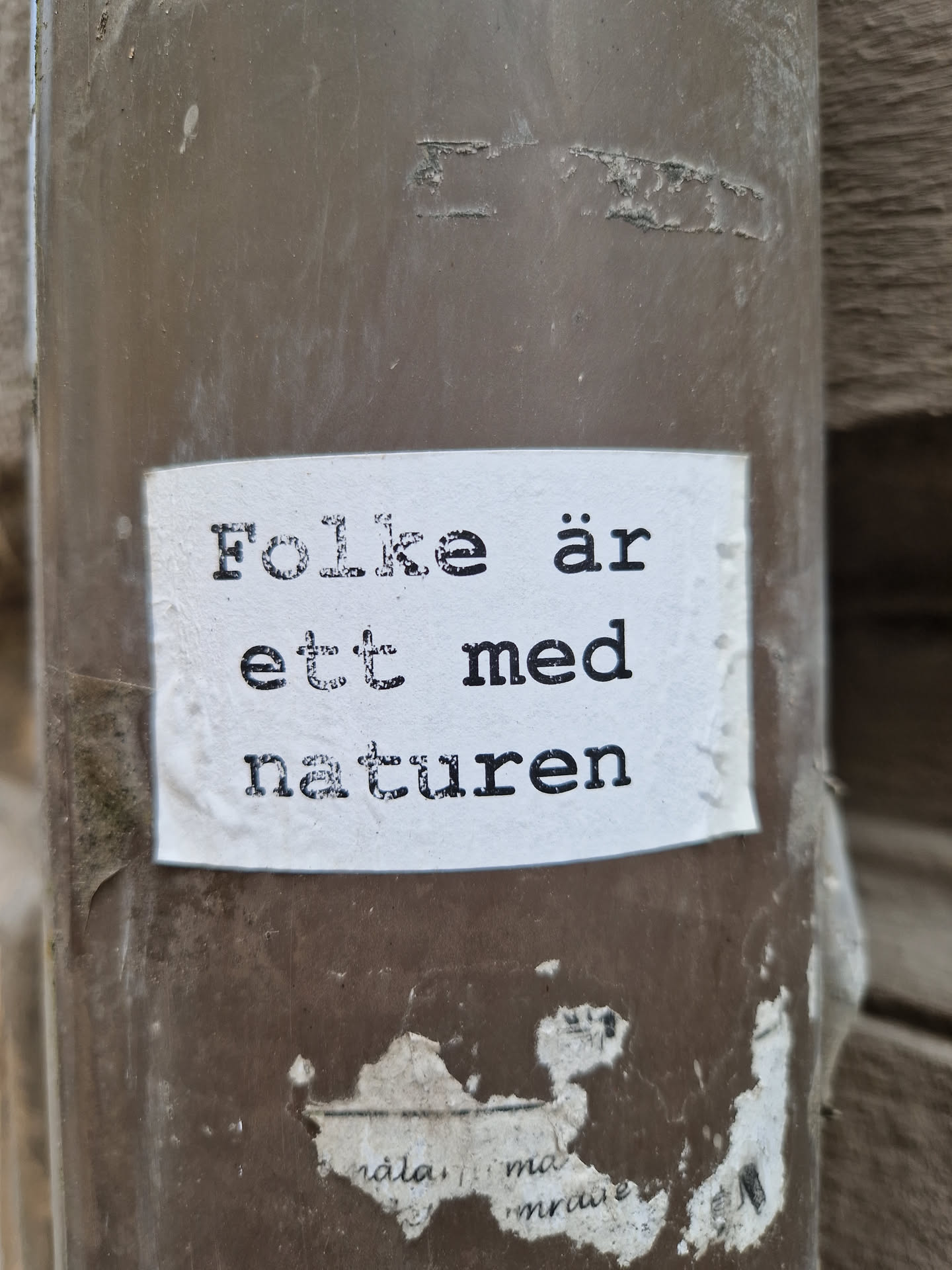A sticker with the text "Folke är ett med naturen" (People are one with nature) in Swedish, attached to a brown pipe.