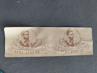 A beige sticker featuring a repeating design. Each element includes a portrait of a man with a beard and glasses set within a circular frame, accented by ornate flourishes. A banner beneath reads "mrchai.se". The overall aesthetic is vintage or retro.