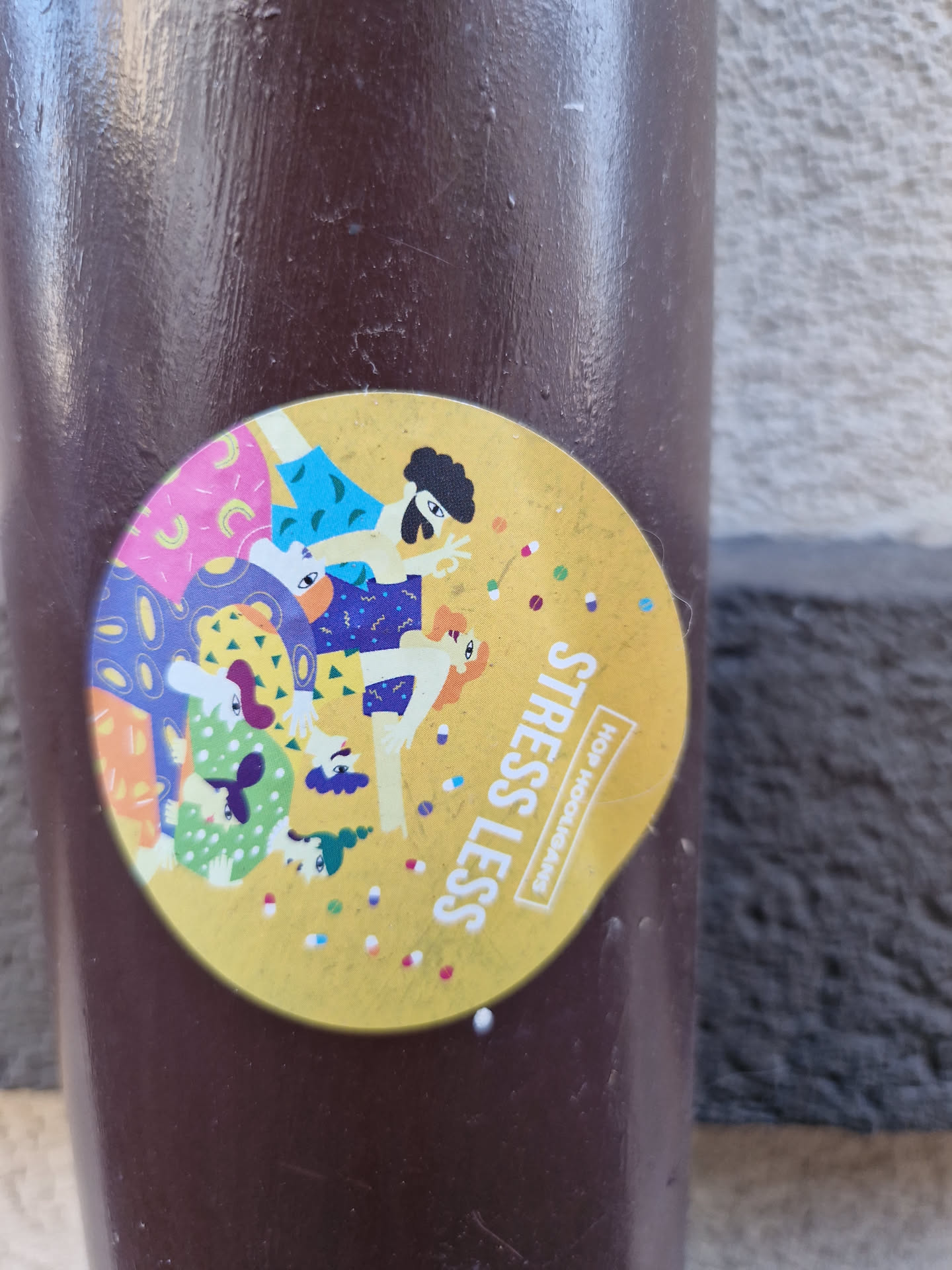 Round yellow sticker with illustration of people and colorful dots. Text on the sticker says "Stress Less" and "HOP Headphones".
