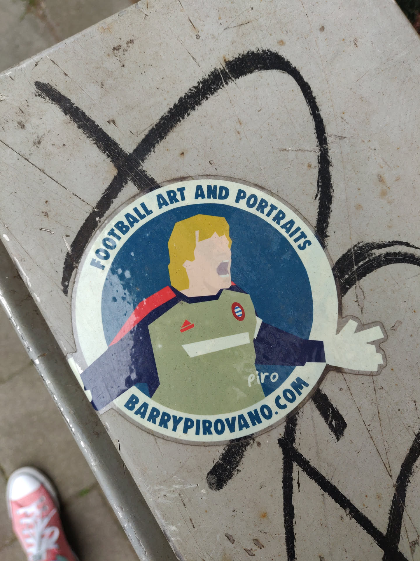 A sticker featuring an illustration of a blond footballer in a retro-style kit. The design is minimalist and colorful, with a circular border containing the artist's name and website address.