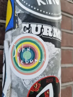 Round sticker with a rainbow-like concentric circle design. The name John Lebanon is written in a stylized script within the circles.