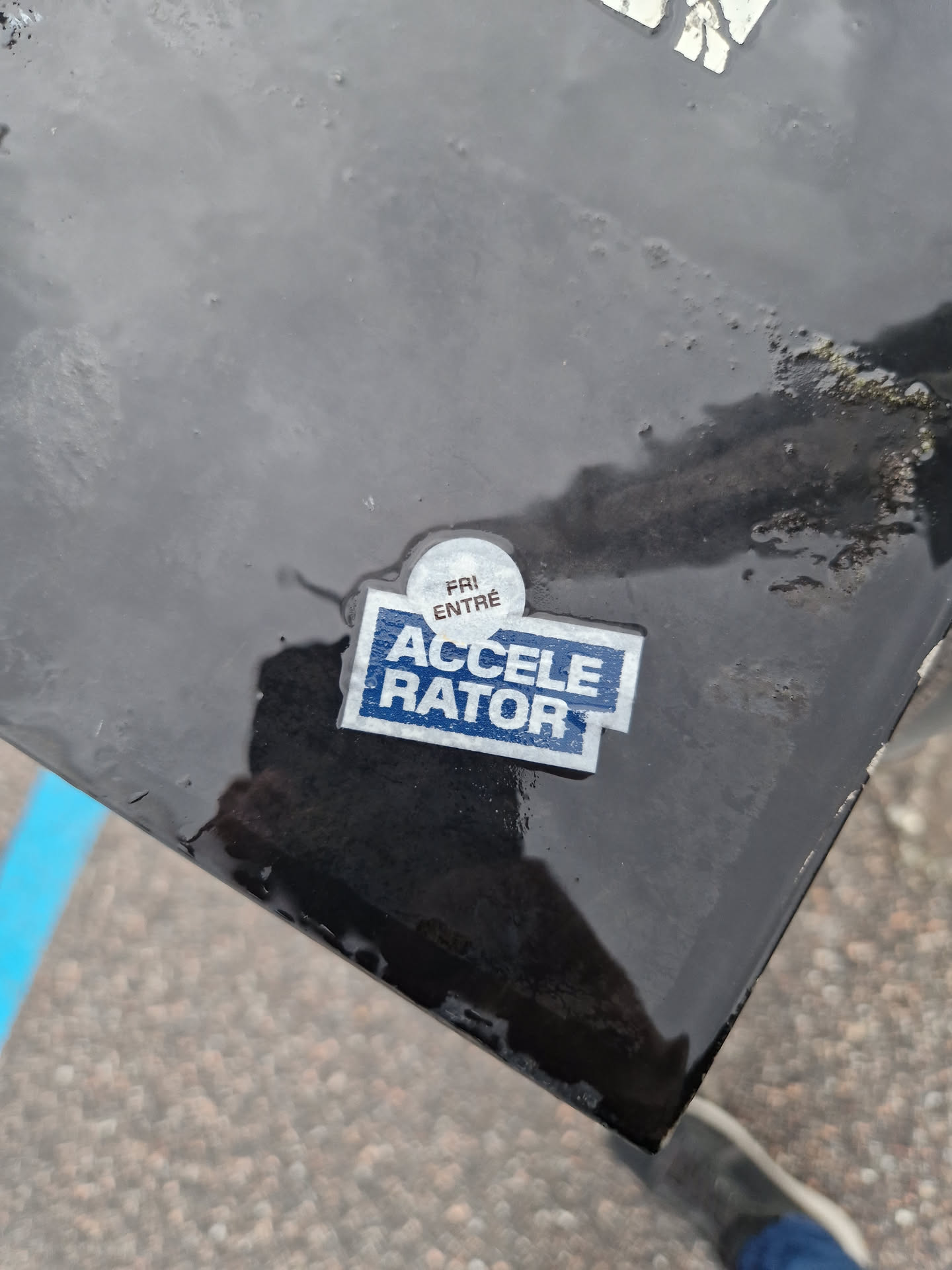 A small, blue and white sticker with the word "ACCELERATOR" in bold, white capital letters.  There is also a smaller, circular sticker on top that says "FRI ENTREE" in smaller letters.
