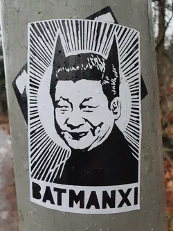 Black and white sticker depicting Xi Jinping with Batman ears. The text at the bottom reads "BATMANXI".