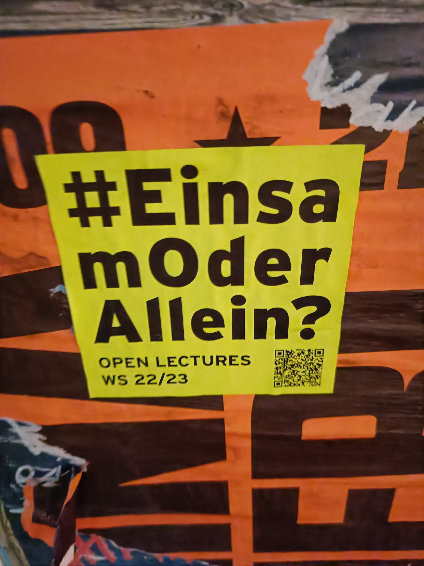 Yellow sticker with black text. The text says #EinsamOderAllein? and below it says Open Lectures WS 22/23. There is also a QR code on the sticker.