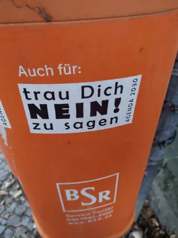 A sticker on an orange bin with the text \"trau Dich NEIN! zu sagen\" (Dare to say NO!) in bold black letters.  The sticker also contains the small print \"AGENDA 2030\" in the upper right corner. The background is an orange bin with the BSR logo and contact details.