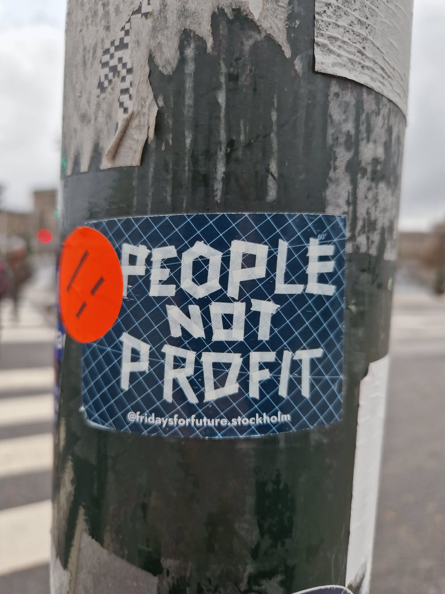 A sticker with the text "PEOPLE NOT PROFIT" on a blue background with a grid pattern.  There is a small orange circle with two parallel lines in the upper left corner. The text ©fridaysforfuture.stockholm is visible at the bottom.