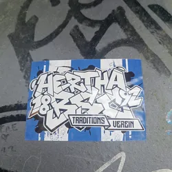 A sticker featuring graffiti-style lettering that says "Hertha 1892" with "Traditions Verein" written underneath in a banner. The sticker has a blue and white color scheme, reminiscent of the Hertha BSC football club's colors. The style is bold and expressive, typical of graffiti art.