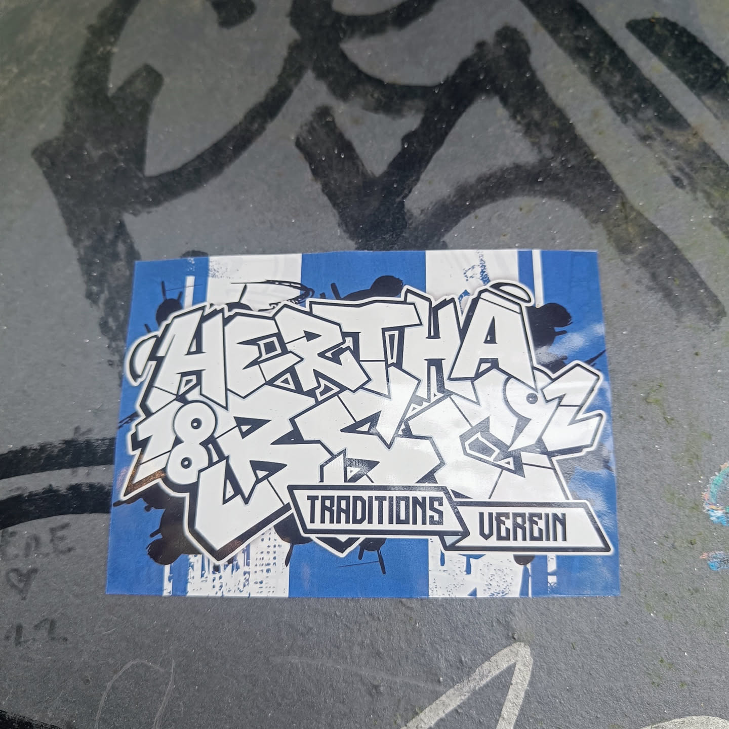 A sticker featuring graffiti-style lettering that says "Hertha 1892" with "Traditions Verein" written underneath in a banner. The sticker has a blue and white color scheme, reminiscent of the Hertha BSC football club's colors. The style is bold and expressive, typical of graffiti art.