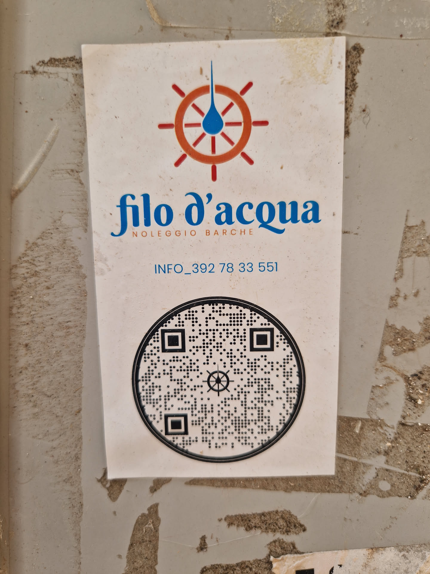 A sticker for Filo d'acqua, a boat rental service.  The sticker features a logo with a water droplet in a ship's wheel and a QR code.  Contact information is also included.