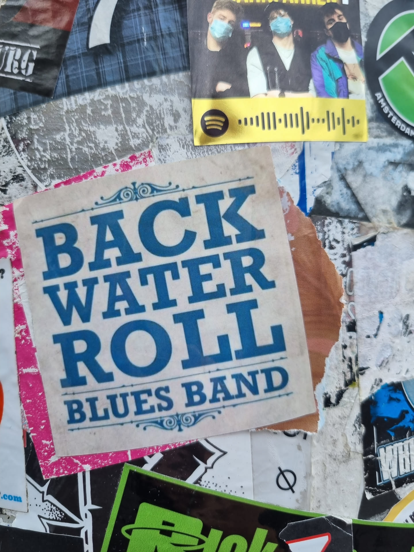 A sticker featuring the name of a blues band, \"Backwater Roll Blues Band\", in a vintage style. The text is blue on a pink and beige background.