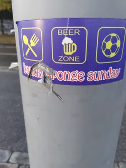 A partially torn sticker promoting a Beer Zone with food and table football, specifically mentioning "Banca Sponge Sunday". The sticker features icons for cutlery, beer, and a soccer ball.