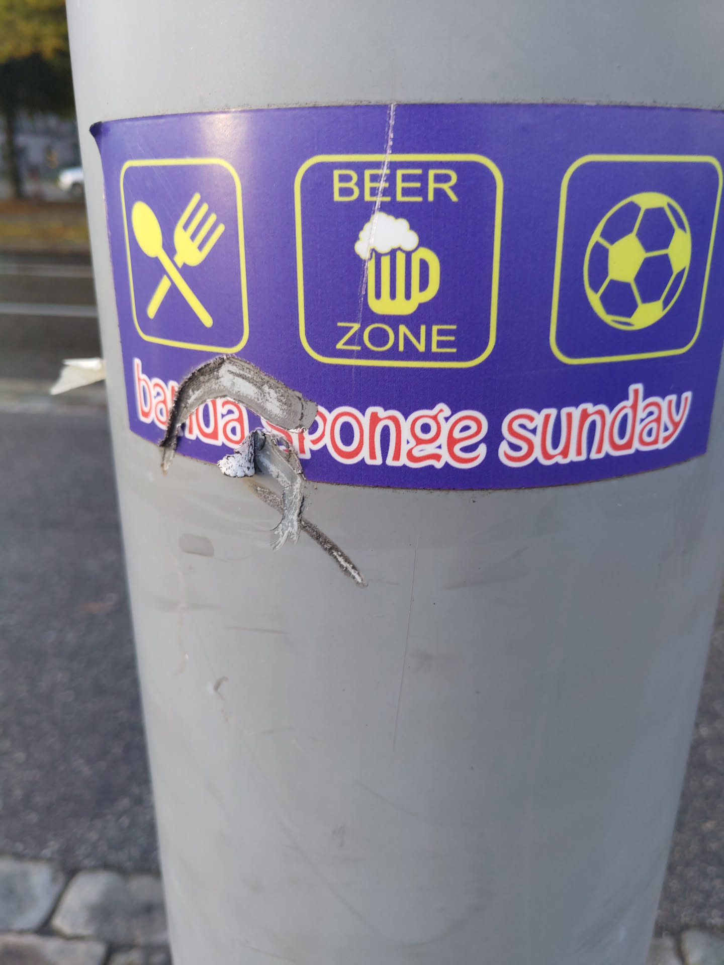 A partially torn sticker promoting a Beer Zone with food and table football, specifically mentioning "Banca Sponge Sunday". The sticker features icons for cutlery, beer, and a soccer ball.