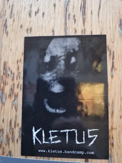 A black and white sticker featuring a dark, ghostly face with a slight smile. The band name \"KLETUS\" is written below the image in a stylized font. A website address is also visible at the bottom.
