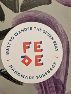 Round sticker with a logo and text. The logo is composed of stylized letters F, E, and E. The text around the logo says: "Built to wander the seven seas | FEE | Handmade surfbags"