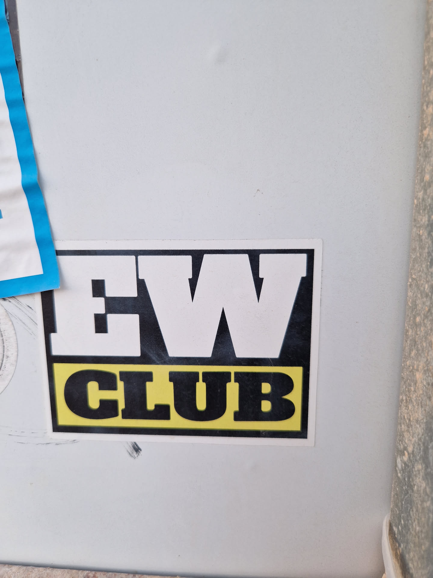 A black and yellow sticker with the text "EW CLUB" in bold, uppercase letters. The letters "EW" are larger than the word "CLUB".