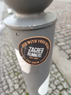A round black and orange sticker on a grey pole.  The text reads: 'Run with your heart' in a circle around the main text: 'Zagreb Runners -Est. 2015- 442 Crew'.