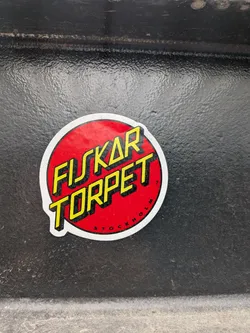 A circular sticker with a vibrant red background. The main text, 'FISKAR TORPET', is prominently displayed in two lines using bold, yellow block letters with a distinct black drop shadow. Below 'TORPET', the word 'STOCKHOLM' is written in smaller, curved black letters, following the bottom arc of the circle. A tiny 'TM' symbol is visible to the right of 'TORPET'. The entire design is framed by a clean white border, giving it a classic, impactful logo appearance.