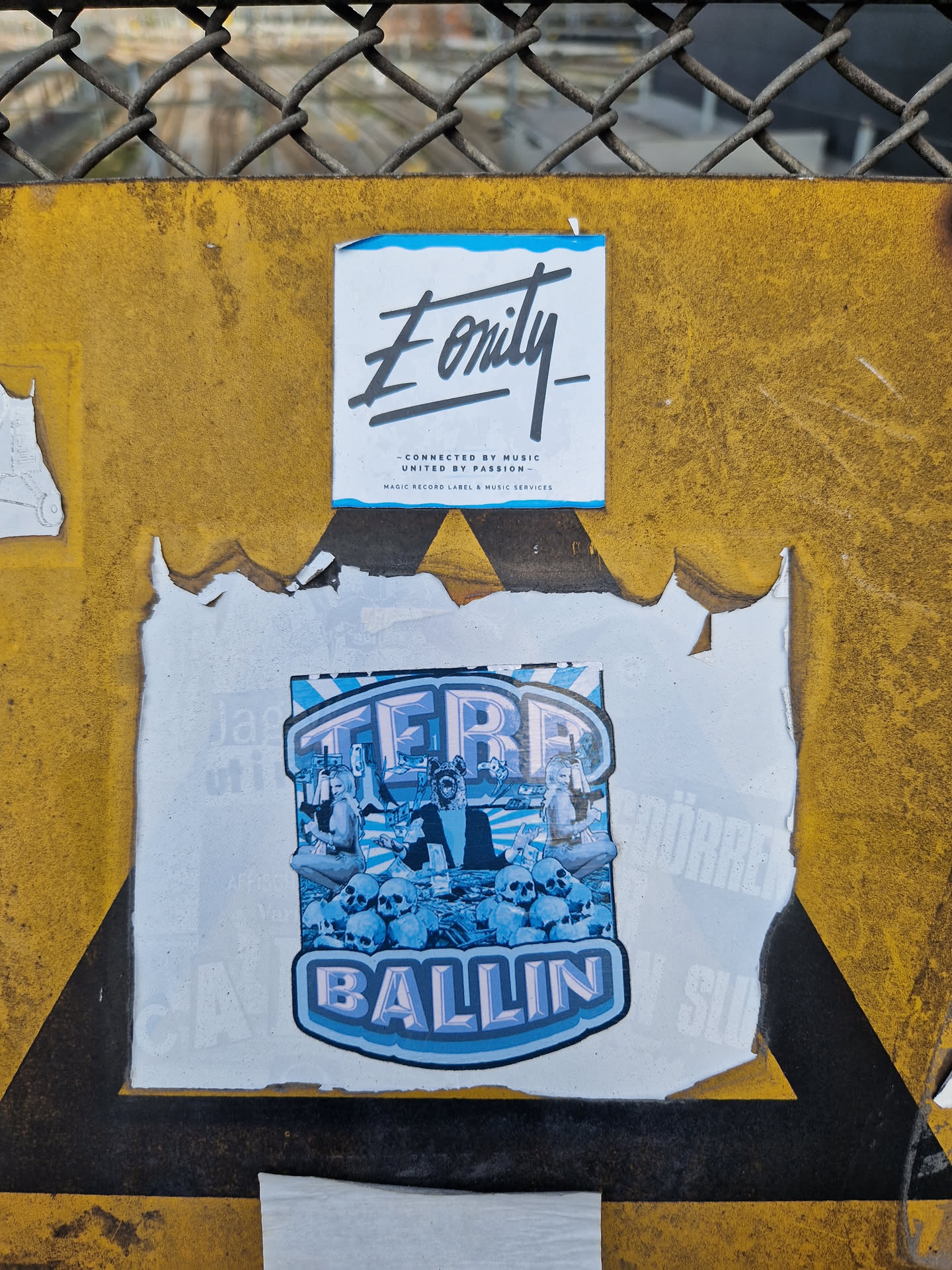 A sticker featuring the text 'TERRA BALLIN' in a stylized font, along with an illustration of what looks like a band or group of people sitting amidst skulls. The color scheme is predominantly light blue and purple. There's a smaller sticker above it with the text 'Eonity' and some additional details.