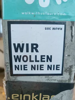 A sticker with the German phrase "Wir wollen nie nie nie" which translates to "We never want never never" in English.  The sticker also has the number "Raum 305" (Room 305) in the top right corner.