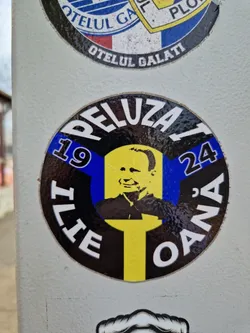 Round sticker with a black background and yellow and blue accents. It features a portrait of Ilie Oana and the text 'Peluza 19 Ilie Oana 24'.