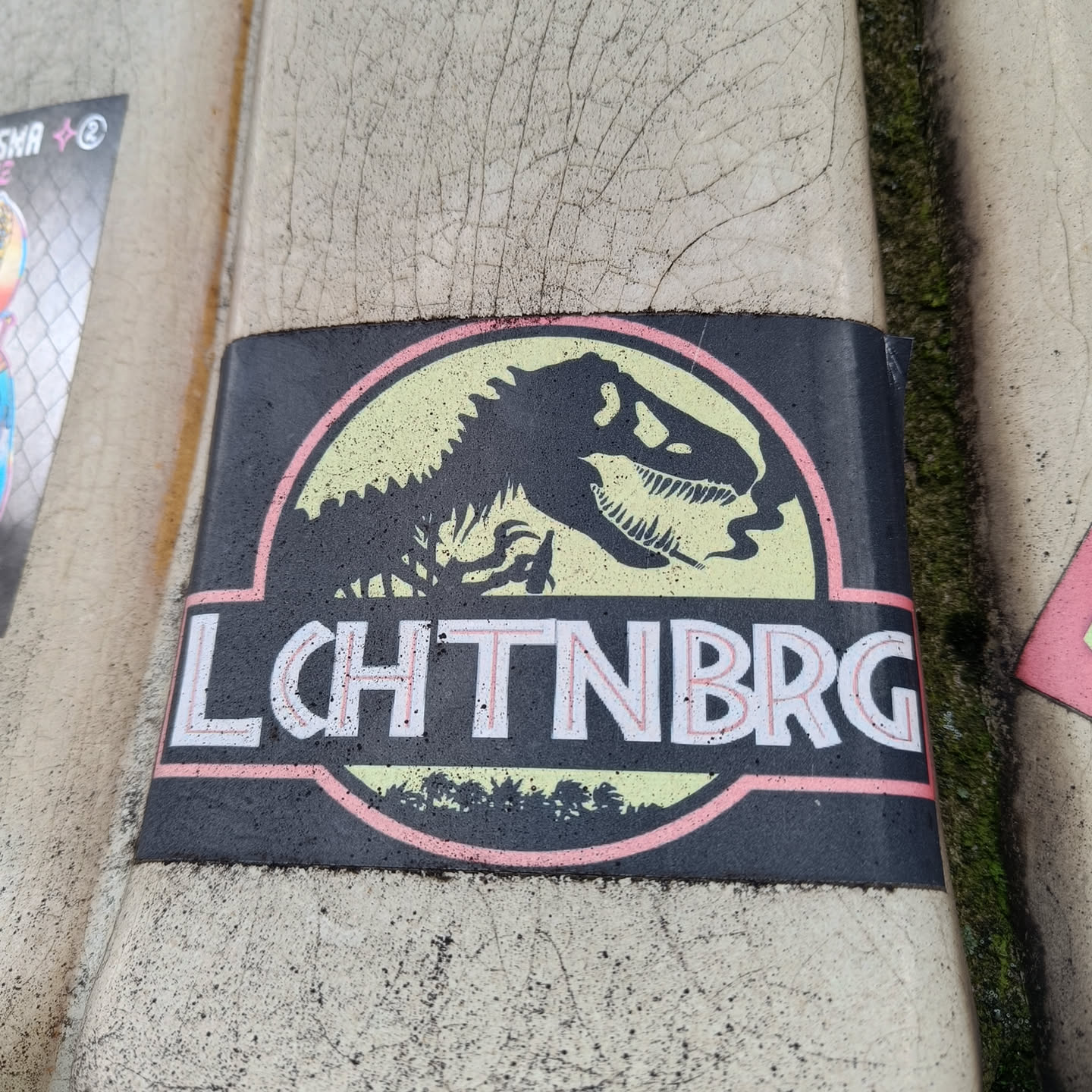 A black sticker with a pale yellow Jurassic Park logo. Instead of the original text, it says LCHTNBRG in a stylized font.
