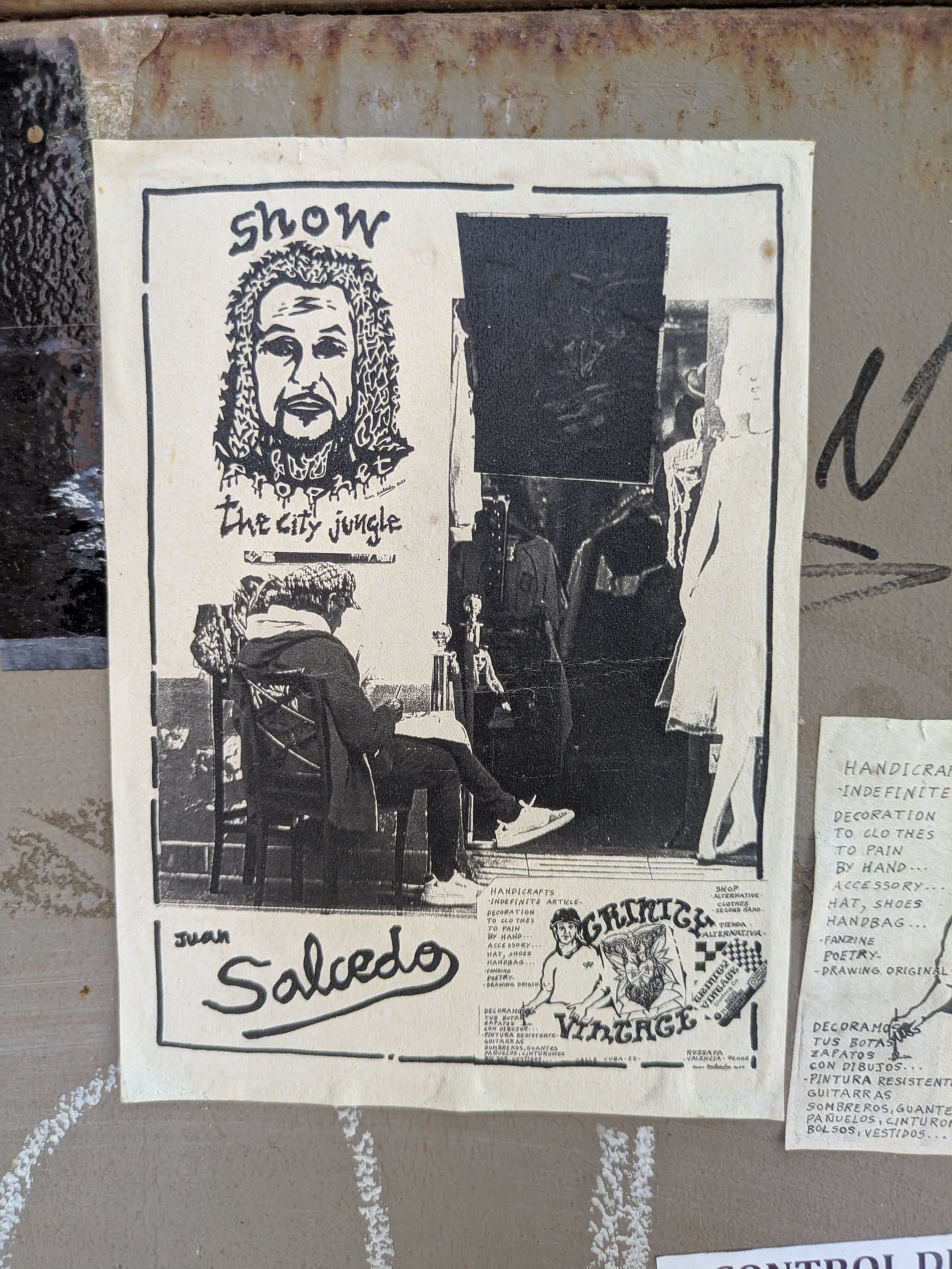 This black and white flyer advertises a show by Juan Salcedo, titled "The City Jungle." It features a portrait at the top and an image of someone sitting in a chair. It also includes information about handicrafts, alternative clothing, and the Grinch Vintage brand. The flyer mentions Russafa, Valencia.