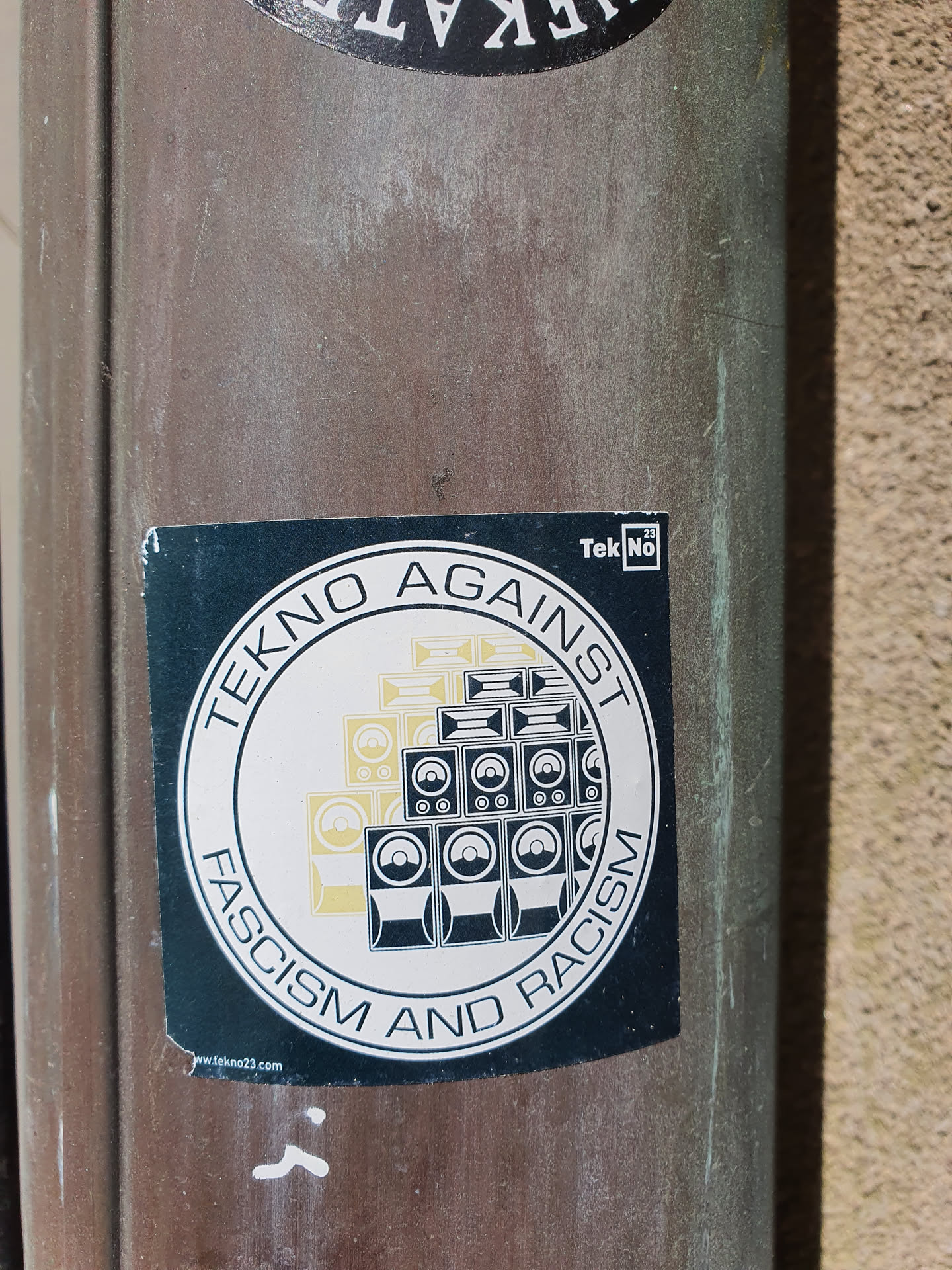 A round sticker with the text 'TEKNO AGAINST FASCISM AND RACISM' surrounding an image of a stack of speakers.  The sticker has a website address at the bottom.