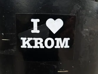 A black and white sticker with the text "I ♥ KROM" on it. The sticker is attached to a dark surface.