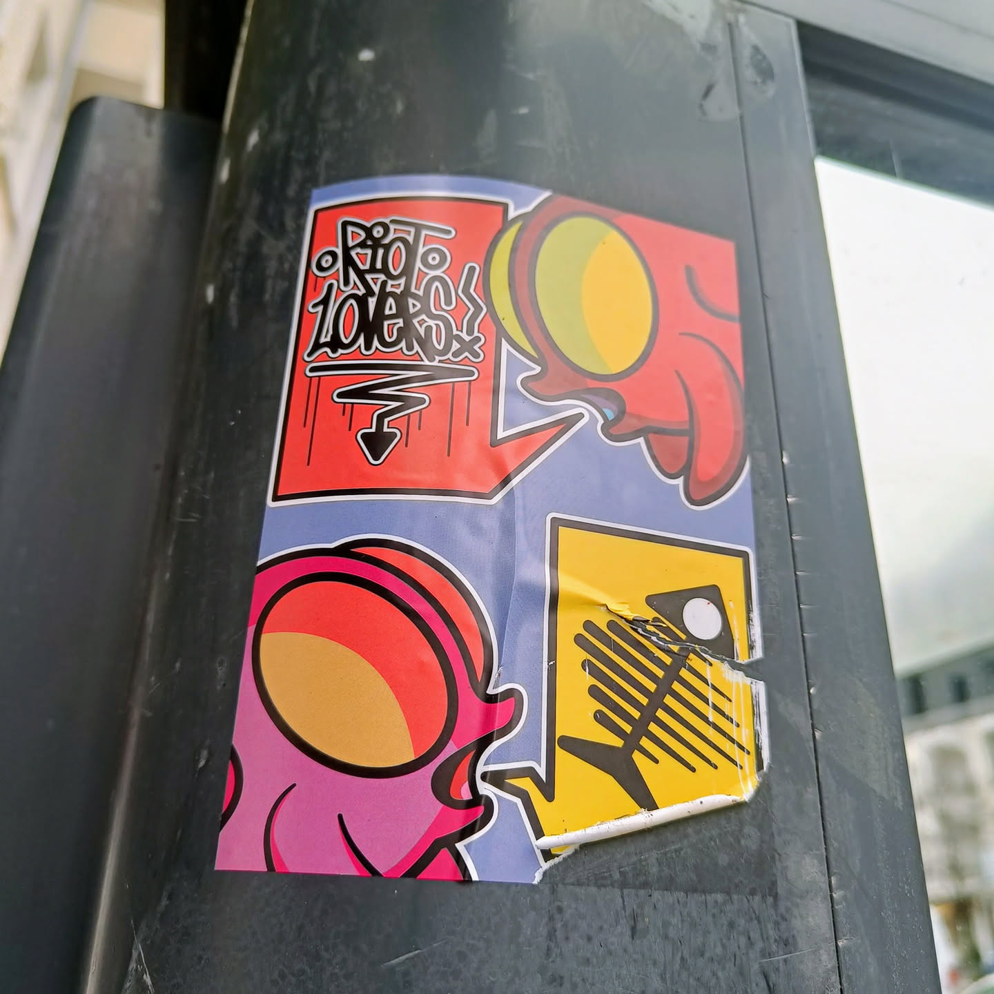 A colorful sticker featuring various cartoonish designs.  The main focus is a pink creature with a round head, accompanied by other smaller illustrations including a red creature and a fish skeleton. One speech bubble says "Rio Lovers".