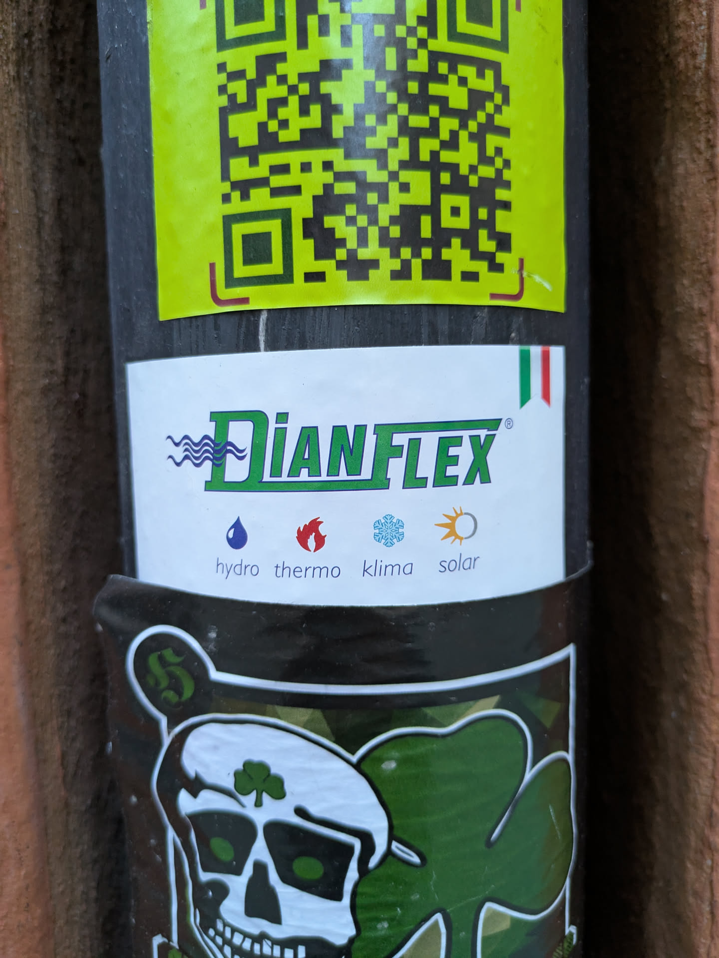 A Dianflex sticker featuring their logo and a skull with a shamrock on its forehead. The sticker is placed on a pole with a QR code above it.