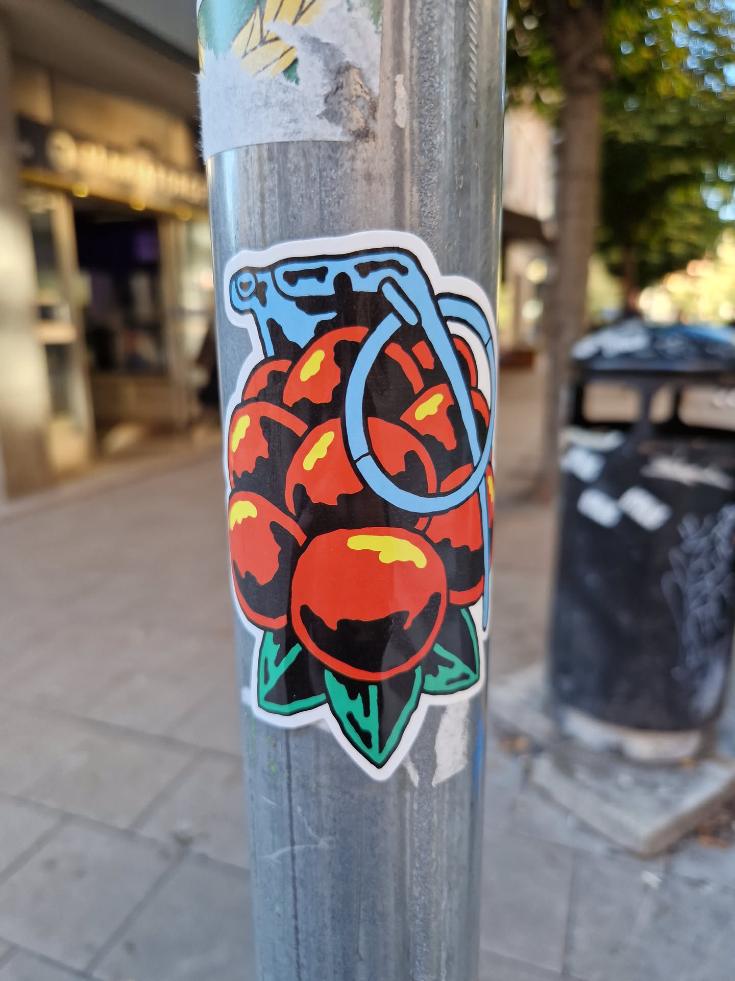 A sticker depicting a grenade-like object filled with red fruits, with green leaves at the bottom and a light blue handle. The style is reminiscent of traditional tattoo art.