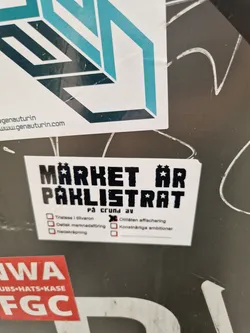 A sticker with text in Swedish that says "MÄRKET ÄR PAKLISTRAT" which translates to "The brand is off the list". It also contains a list of reasons why it might be off the list. The design uses a pixelated font and includes stars.