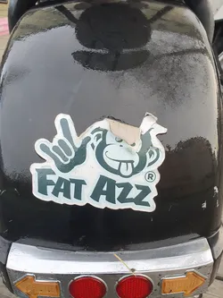 A sticker featuring a cartoon monkey making a rock-on hand gesture with the text 'FAT AZZ' underneath. The sticker appears to be slightly worn or damaged around the edges.