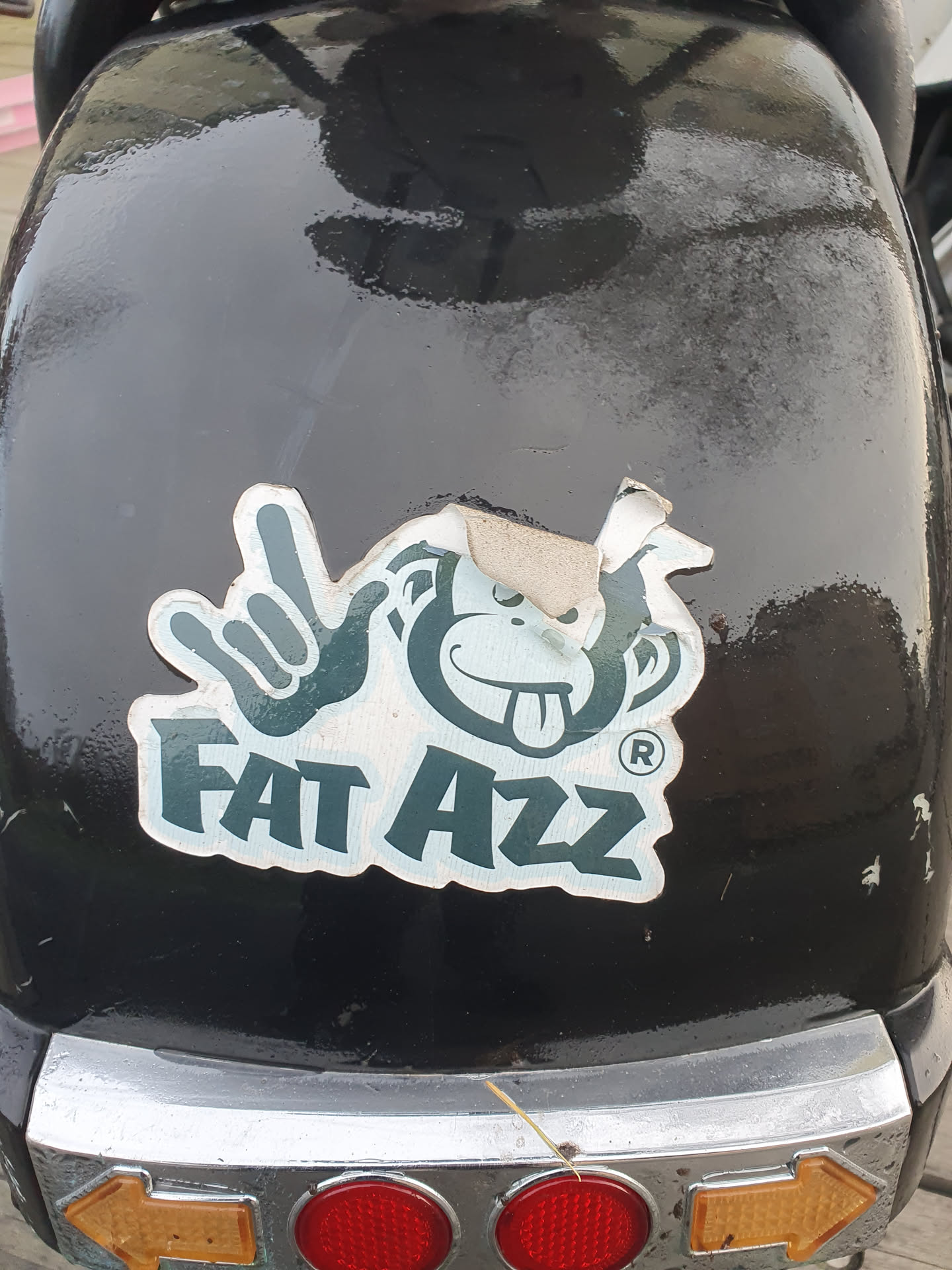 A sticker featuring a cartoon monkey making a rock-on hand gesture with the text 'FAT AZZ' underneath. The sticker appears to be slightly worn or damaged around the edges.