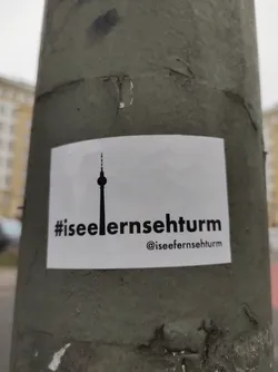 A white sticker with a simple black silhouette of the Berlin Television Tower and the hashtag #iseefernsehturm.  An Instagram handle is also included.