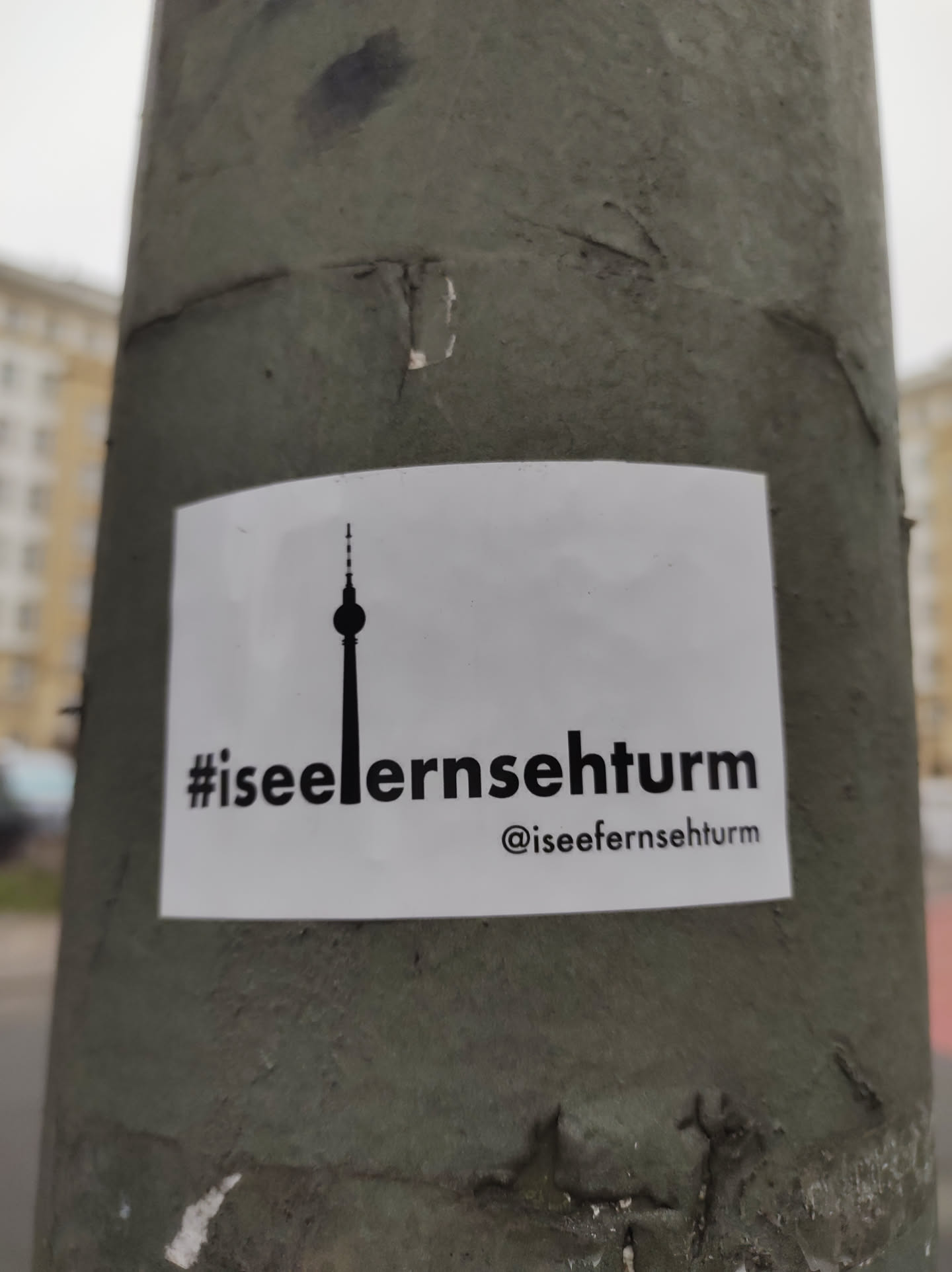 A white sticker with a simple black silhouette of the Berlin Television Tower and the hashtag #iseefernsehturm.  An Instagram handle is also included.