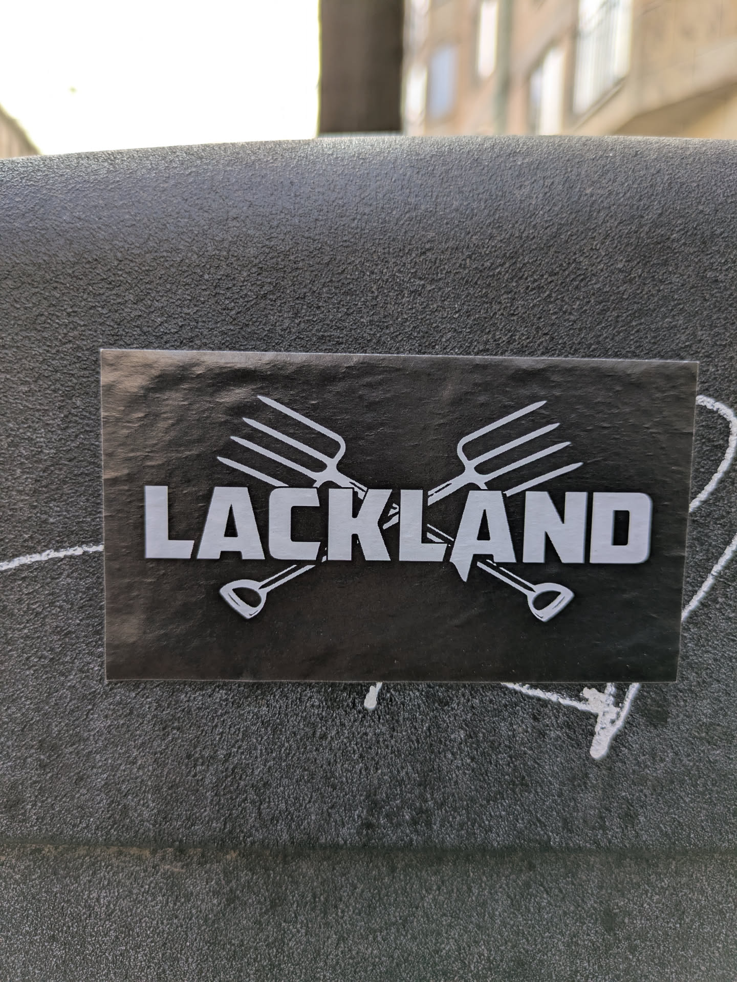 A black sticker shows the word "LACKLAND" in bold white letters, set against two crossed gardening tools - a garden fork and a shovel.