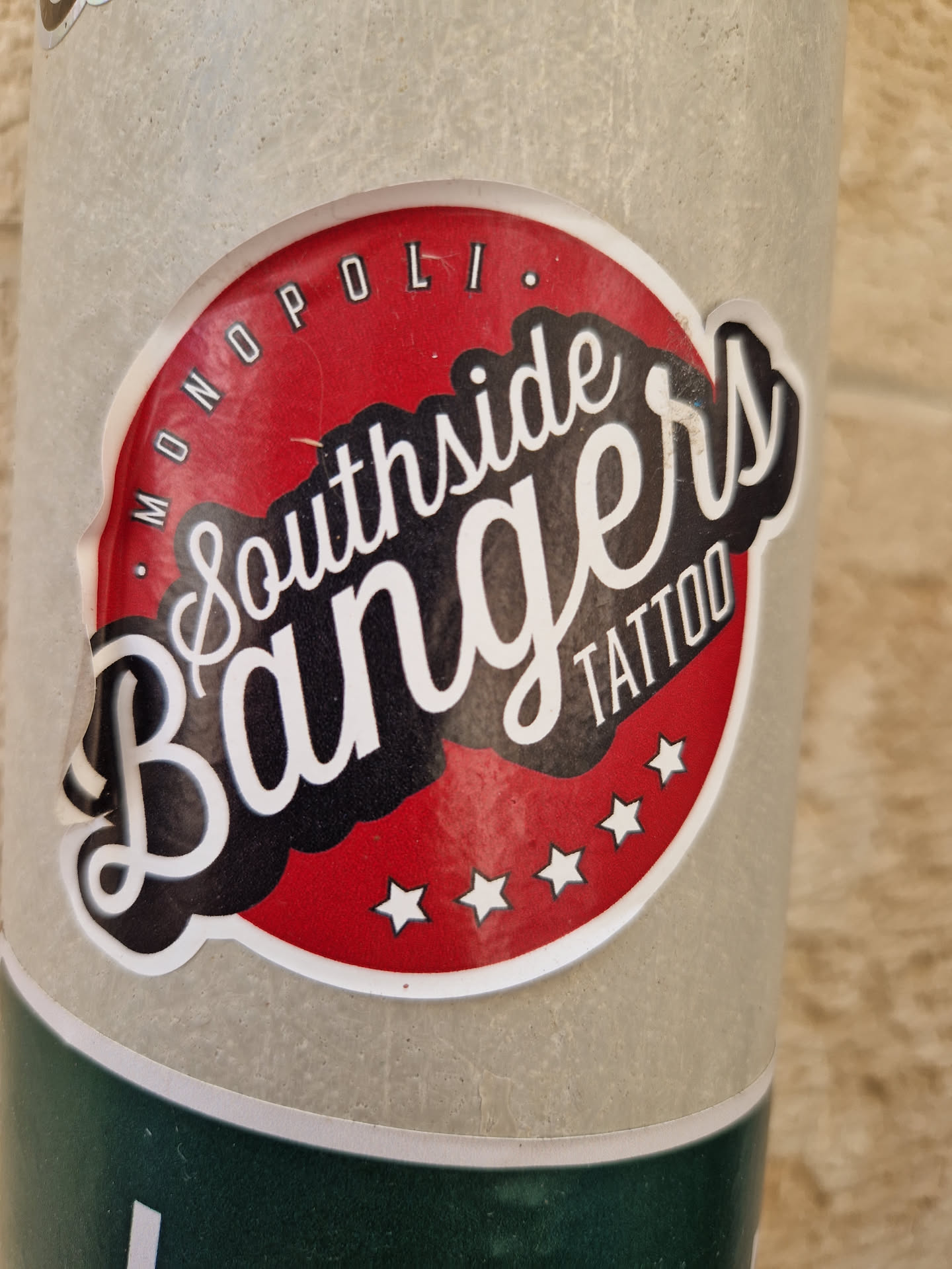 A round sticker with a red background and white stars. The text "Southside Bangers Tattoo" is written in a stylized font, with the words "Monopol." written in small letters around the top. 