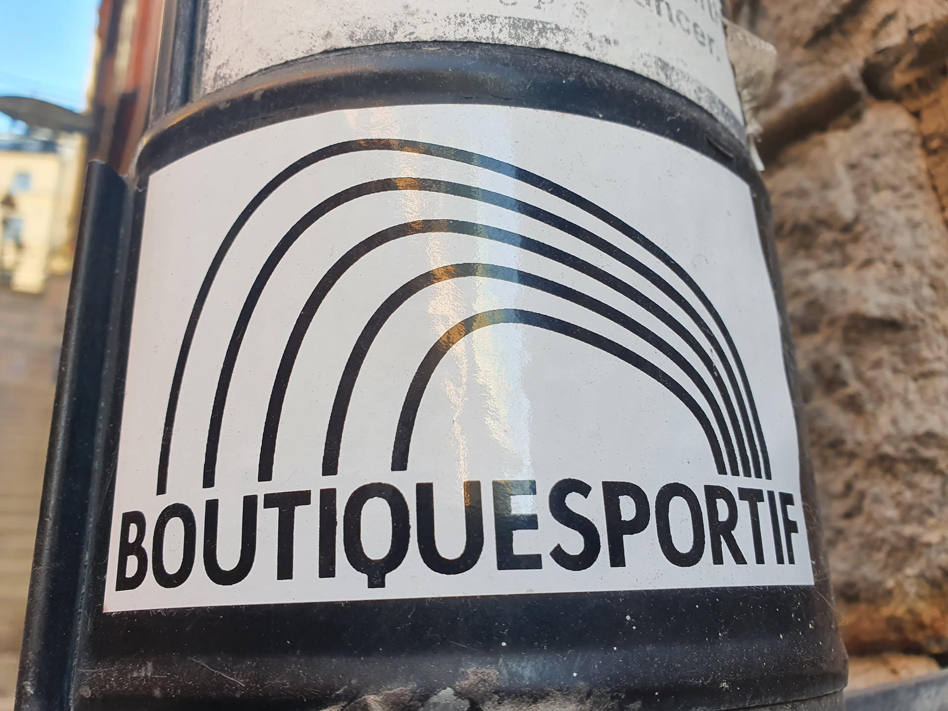 The sticker features a stylized rainbow made of five bold black arcs on a white background. Below the rainbow, the text "BOUTIQUESPORTIF" is printed in a sans-serif font.