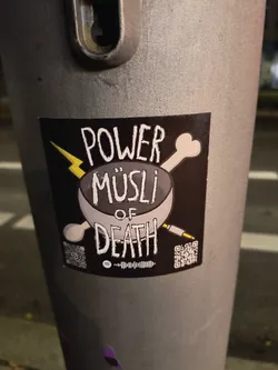 The sticker is rectangular with a black background. At its center, a grey bowl is depicted, filled with what appears to be cereal. A white stylized bone crosses behind the bowl from the upper right, and a yellow audio jack crosses from the lower right. A yellow lightning bolt strikes from the upper left. The text 'POWER MÜSLI OF DEATH' is prominently displayed in a distressed white font, with 'POWER' at the top, 'MÜSLI' in the bowl, and 'OF DEATH' below the bowl. Below the main design, there's a Spotify code in the center, flanked by two QR codes. The left QR code contains a small Instagram logo in its center.