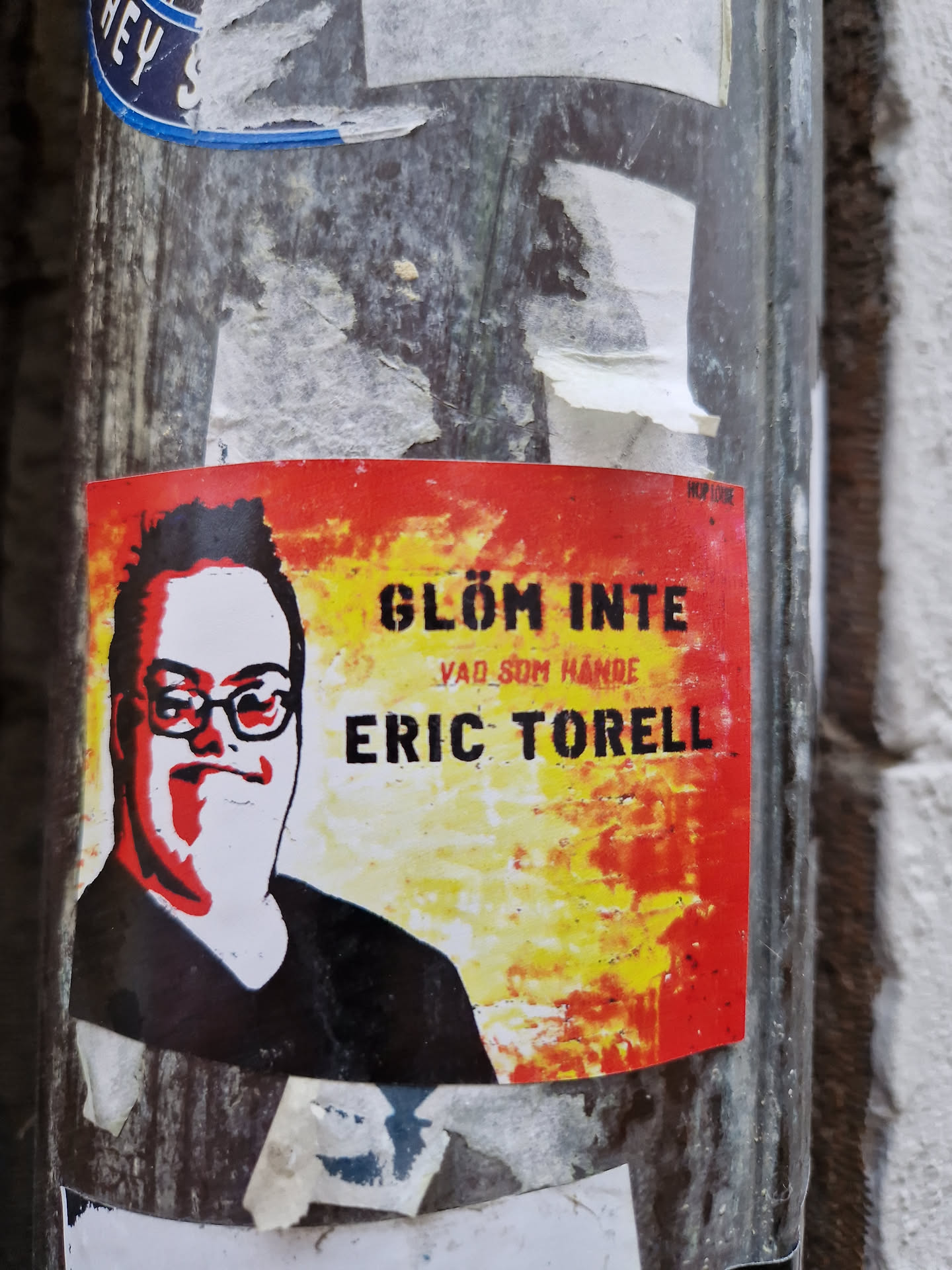 A sticker featuring a stylized portrait of Eric Torell with text that translates to "Don't forget what happened." The background is a fiery mix of red and yellow.