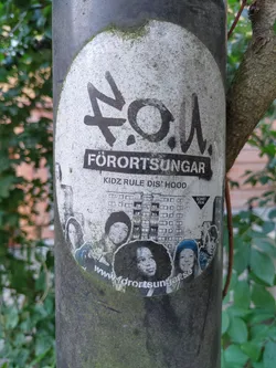 A worn sticker featuring the logo and name of Förortsungar, along with a photo of a group of young people. The website address is visible at the bottom.  The text "Förortsungar" and "Kidz rule dis hood" are clearly visible.